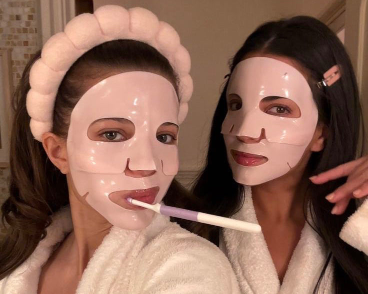 Two women wearing face masks and robes, one holding a toothbrush.